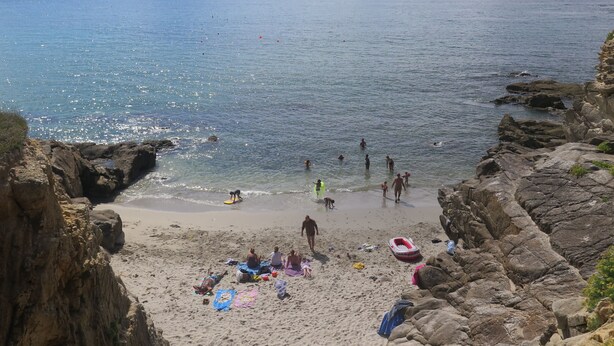 A beach with rocky cliffs, clear blue water, and people enjoying the shore.