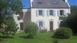 A two-story house with a sloped roof, multiple windows with shutters, and a well-maintained lawn.
