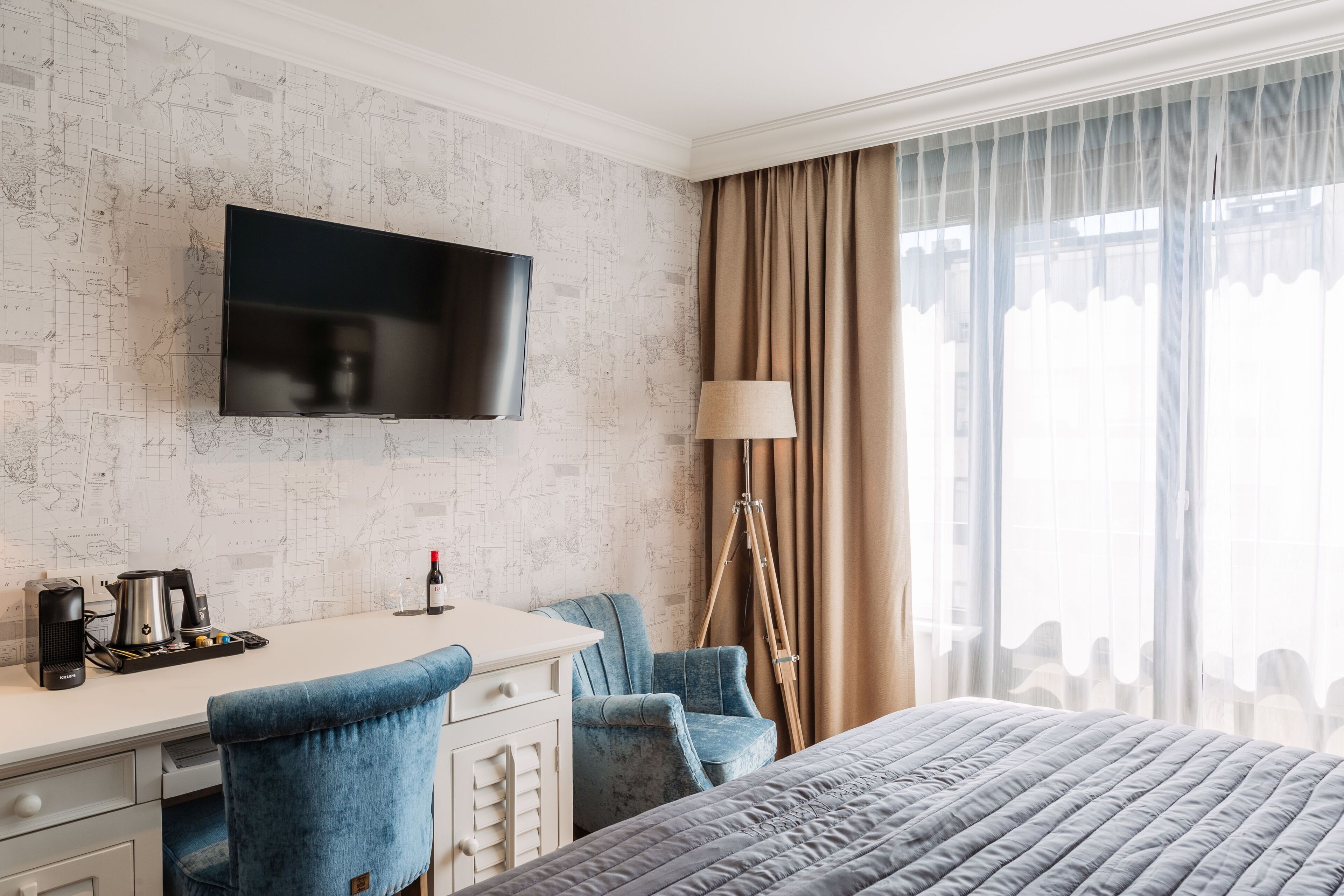 Une chambre d’hôtel équipée d’un téléviseur à écran plat fixé au mur, d’un bureau avec une machine à café, d’une chaise et d’un lit recouvert d’une couverture matelassée.