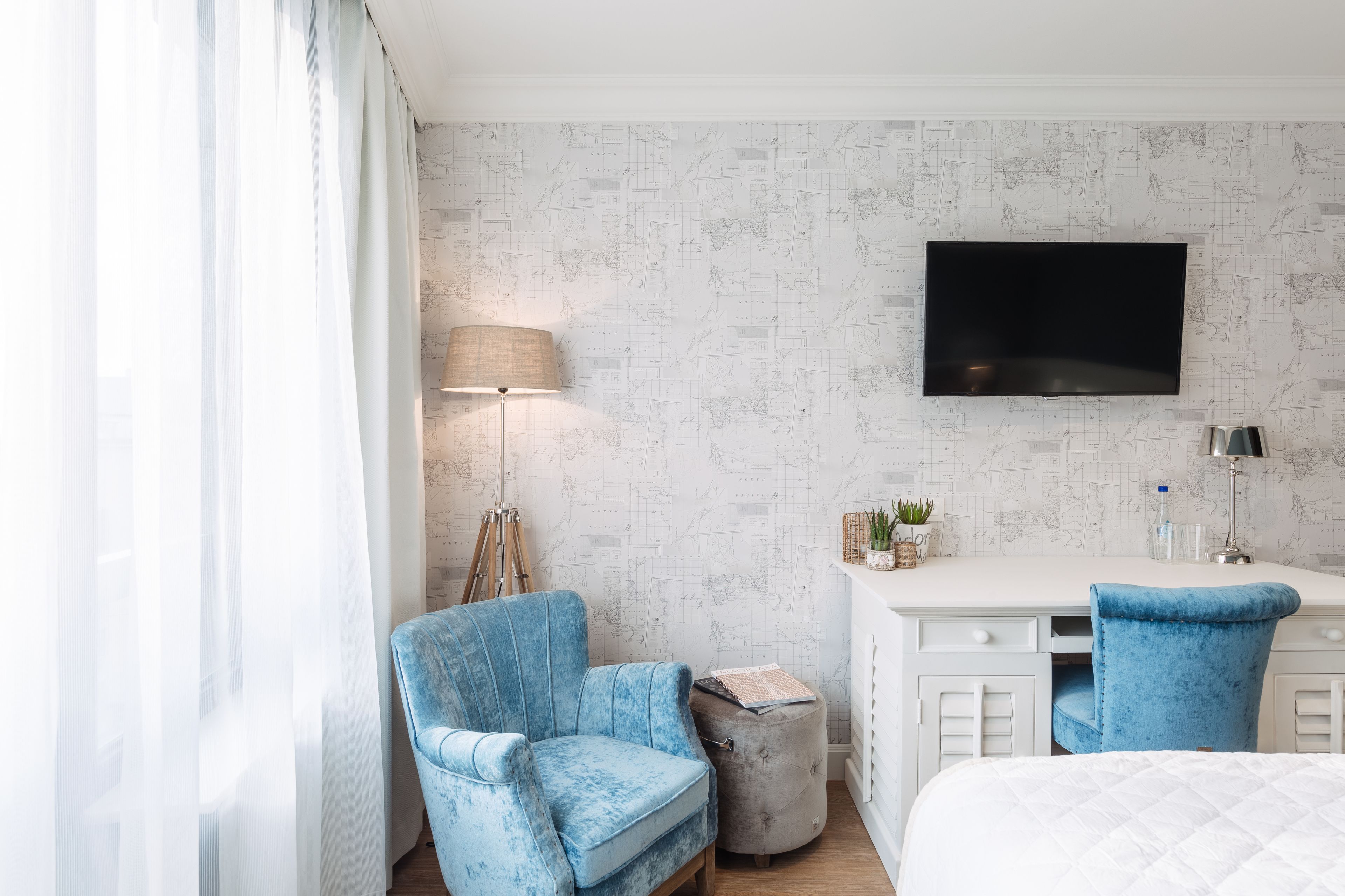 A hotel room with a bed, a desk, a chair, a lamp, and a TV.