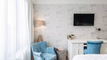 A hotel room with a bed, a desk, a chair, a lamp, and a TV.