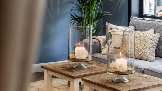 A cozy seating area with a sofa and two glass candle holders on a wooden table. - Hotel Cocoon (Ostend)