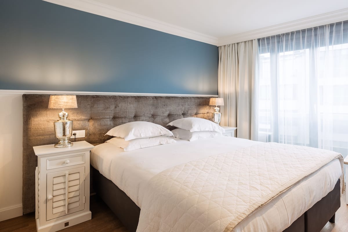 A neatly made bed with a quilted white duvet, a tufted headboard, and two bedside lamps.