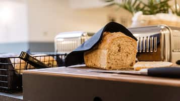 A loaf of bread on a cutting board with a knife, a toaster, and a basket of bread in the background.