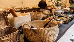 A buffet setup with wicker baskets, a potted plant, and a counter with plates. - Hotel Cocoon (Ostend)