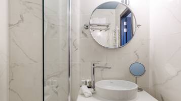 Une salle de bain avec une douche à parois de verre, un lavabo blanc avec un miroir rond et un porte-serviettes.
