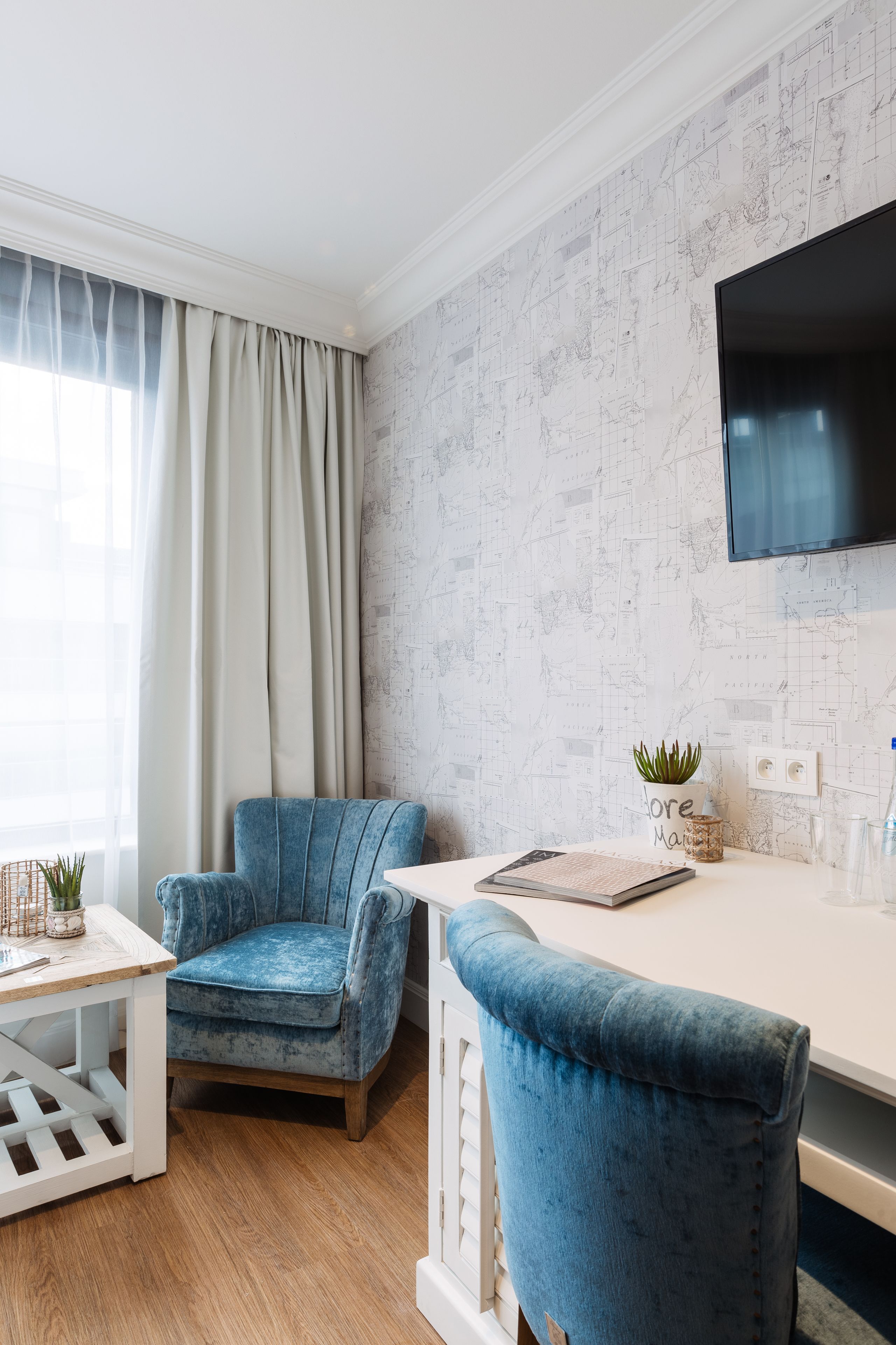 A modern room with a blue armchair, a white desk, and a large TV mounted on the wall.