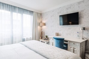 A hotel room with a bed, a desk, a chair, a TV, and a window with curtains. - Hotel Cocoon (Ostend)