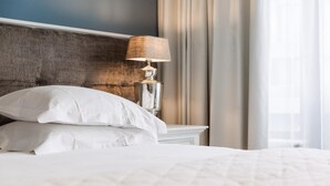 A neatly made bed with white linens and pillows, a classic lamp on a bedside table, and a view of a window with curtains. - Hotel Cocoon (Ostend)