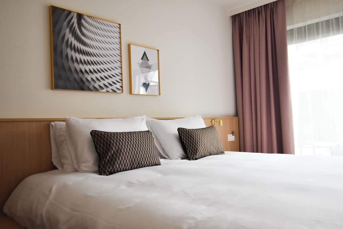 Una cama bien hecha con almohadas blancas y estampadas, un cabecero de madera y dos cuadros enmarcados en la pared.