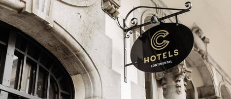A black circular sign with a gold 'C' logo and the text 'HOTELS CONTINENTAL' hanging from a metal bracket on a building facade.