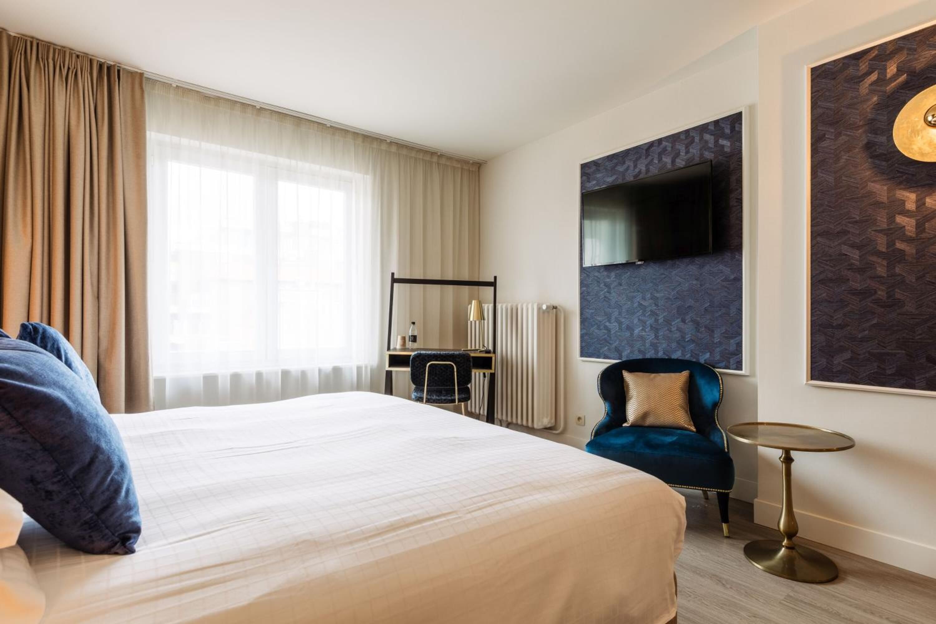 A hotel room with a large bed, a desk, a chair, a TV mounted on the wall, and a round table.