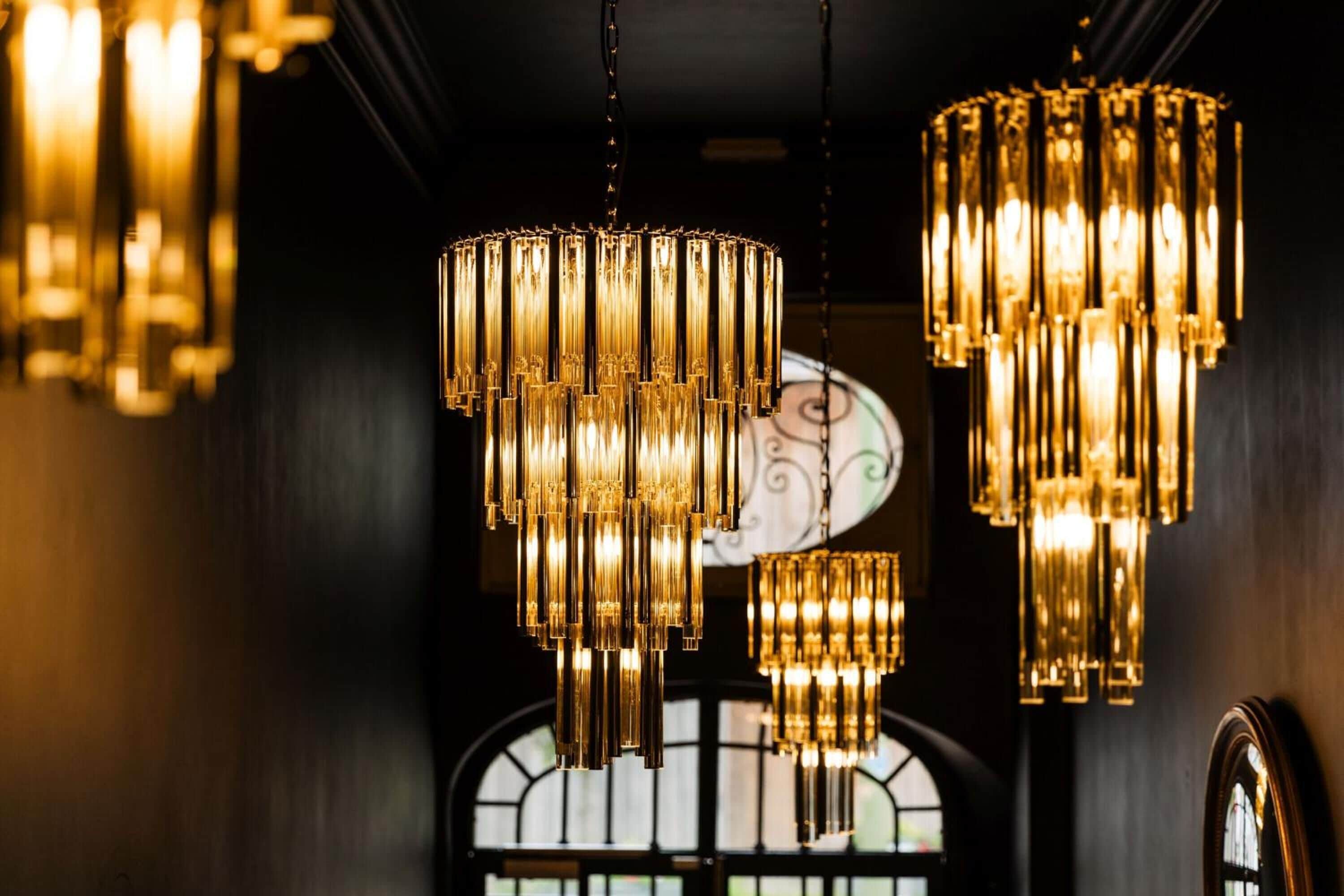 A series of ornate chandeliers hanging from the ceiling in a dimly lit room with arched windows.