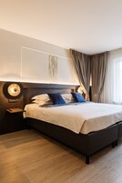Una habitación de hotel moderna con una cama grande, una mesita de noche, una lámpara de pared y una ventana con cortinas.