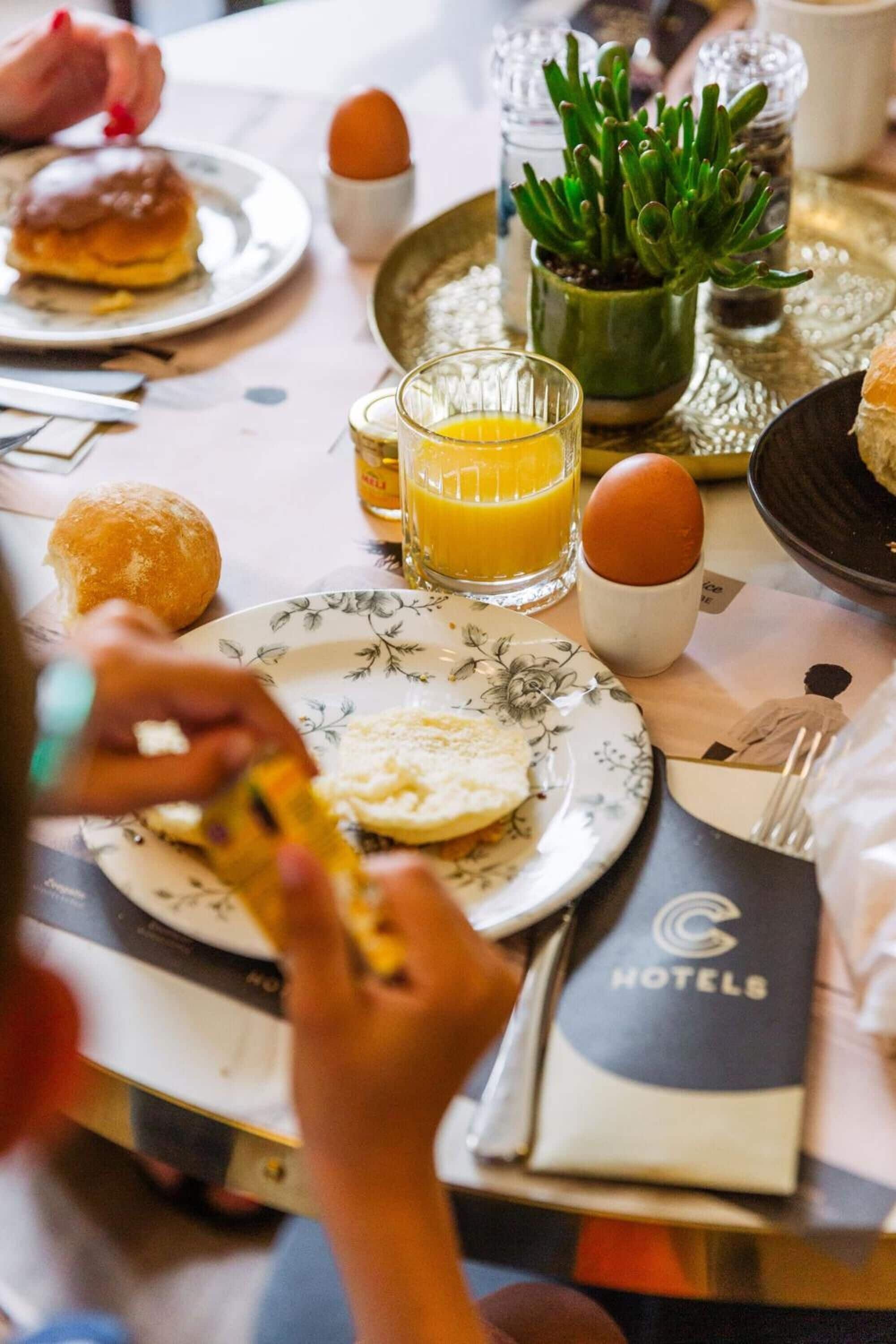 A breakfast setting with plates of food, a glass of orange juice, and a small potted plant on a table.