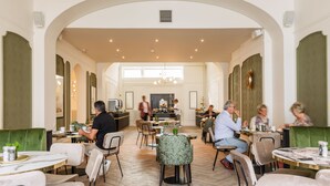 Un vaste espace dédié à la salle à manger, avec de nombreuses tables et chaises, un bar central et un plafond haut doté d’un éclairage encastré.