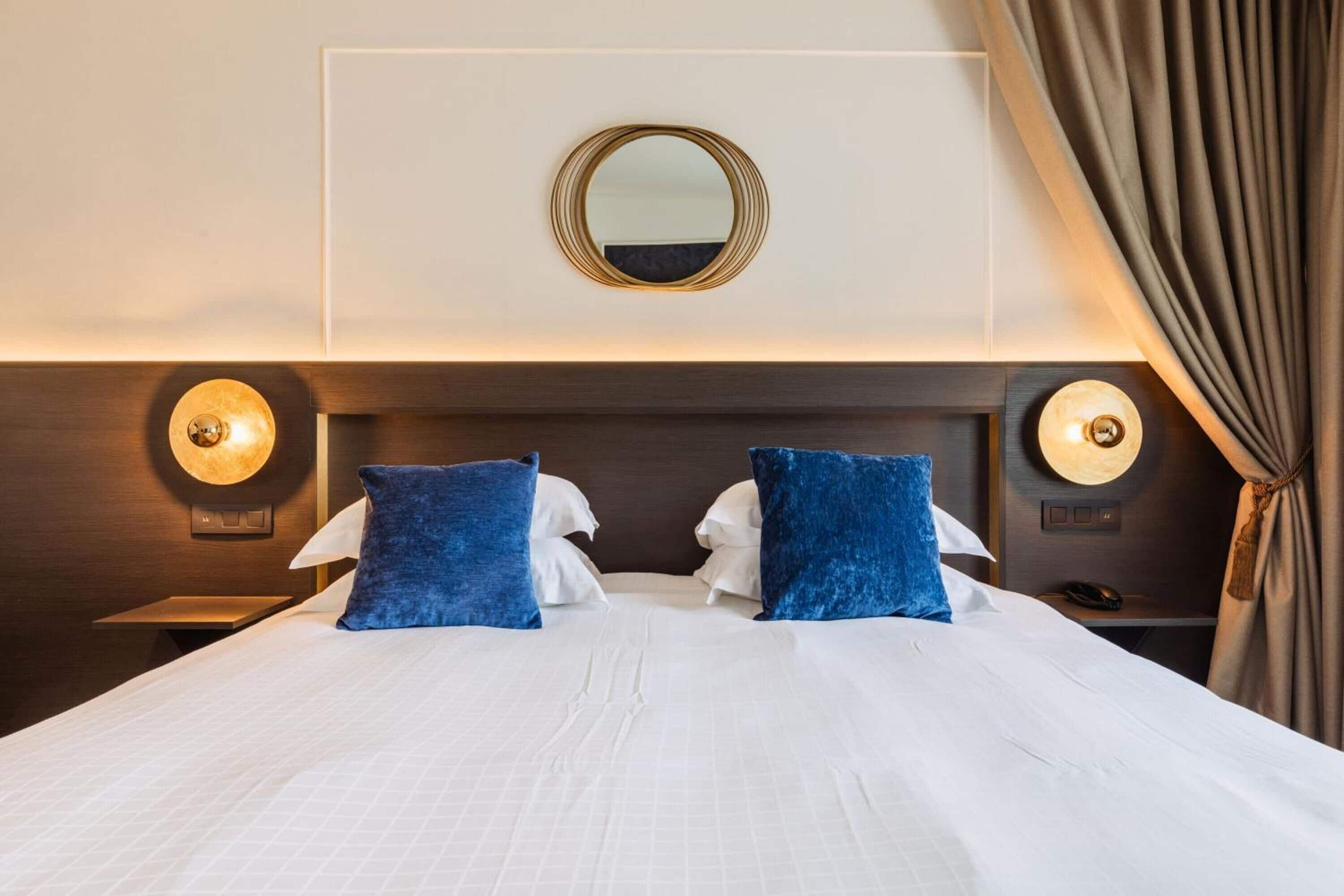 Ein Hotelzimmer mit einem großen Bett, zwei Kissen, einem runden Spiegel und zwei Wandleuchten.