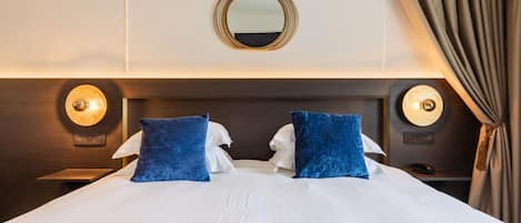 A hotel room with a large bed, two pillows, a round mirror, and two wall sconces.