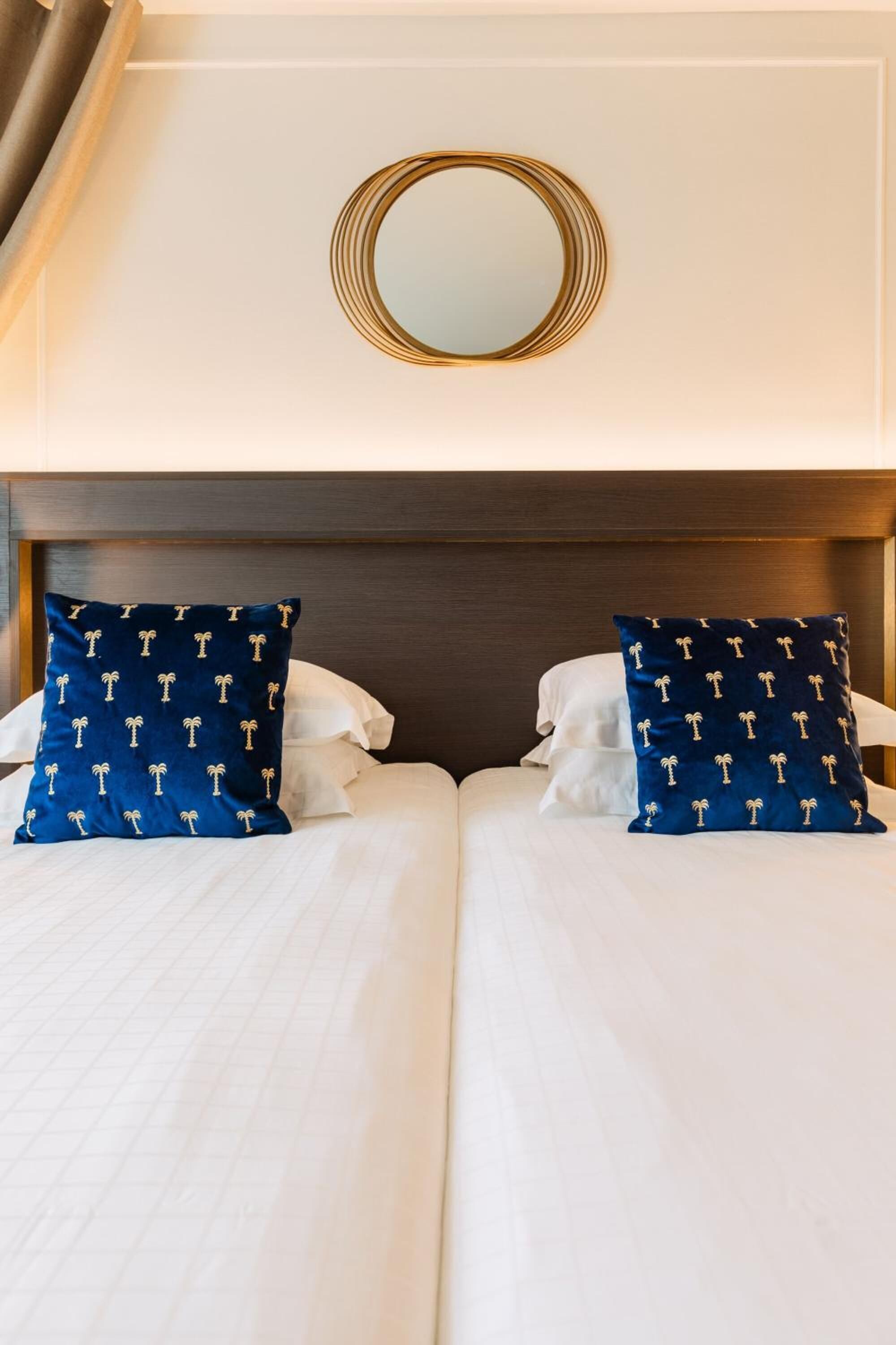 A double bed with white linens and two navy pillows with palm tree patterns.