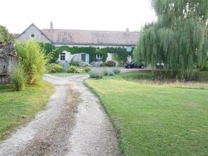 Een grindpad leidt naar een huis met met klimop begroeide muren en een treurwilg.