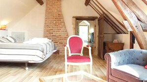 A loft-style bedroom with a sloped ceiling, exposed wooden beams, a brick fireplace, a bed, a red chair, and a blue sofa. - Le Plessis-Le Lierre - Loire Valley-Amboise, 18th Century Farmhouse, Pool (Amboise)