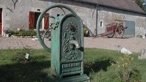 A green water pump with a floral design and the inscription "BEAUNE" in front of a stone building with a red door and a cart in the background. - Le Plessis-Le Lierre - Loire Valley-Amboise, 18th Century Farmhouse, Pool (Amboise)