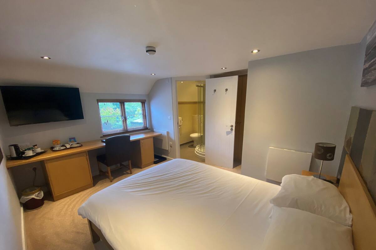 Quarto de hotel moderno com cama, escrivaninha, cadeira, televisão e banheiro.