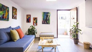 A living room with a blue sofa, a wooden coffee table, and a bench. There are four paintings on the wall and several potted plants. - Old Town Guest Houses (Batroun)