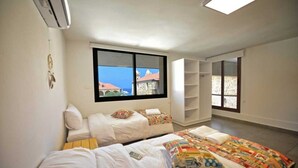 A room with two beds, a large window, and a view of buildings. - Old Town Guest Houses (Batroun)