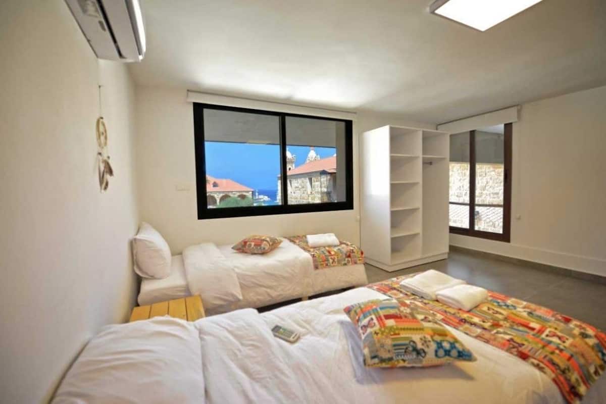 A room with two beds, a large window, and a view of buildings.
