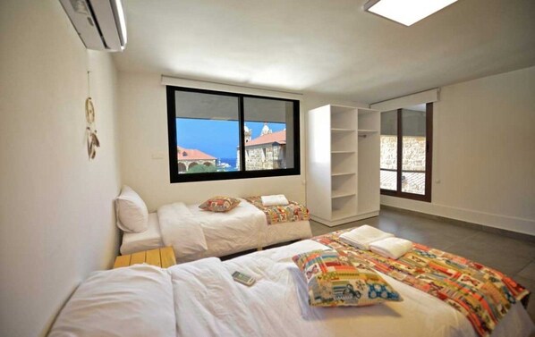 A room with two beds, a large window, and a view of buildings.