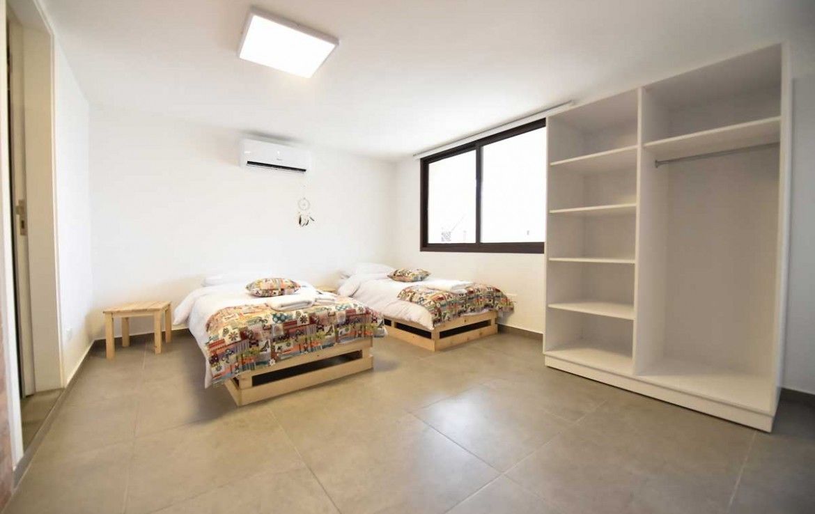 A bedroom with two beds, a wardrobe, a small table, and a window.