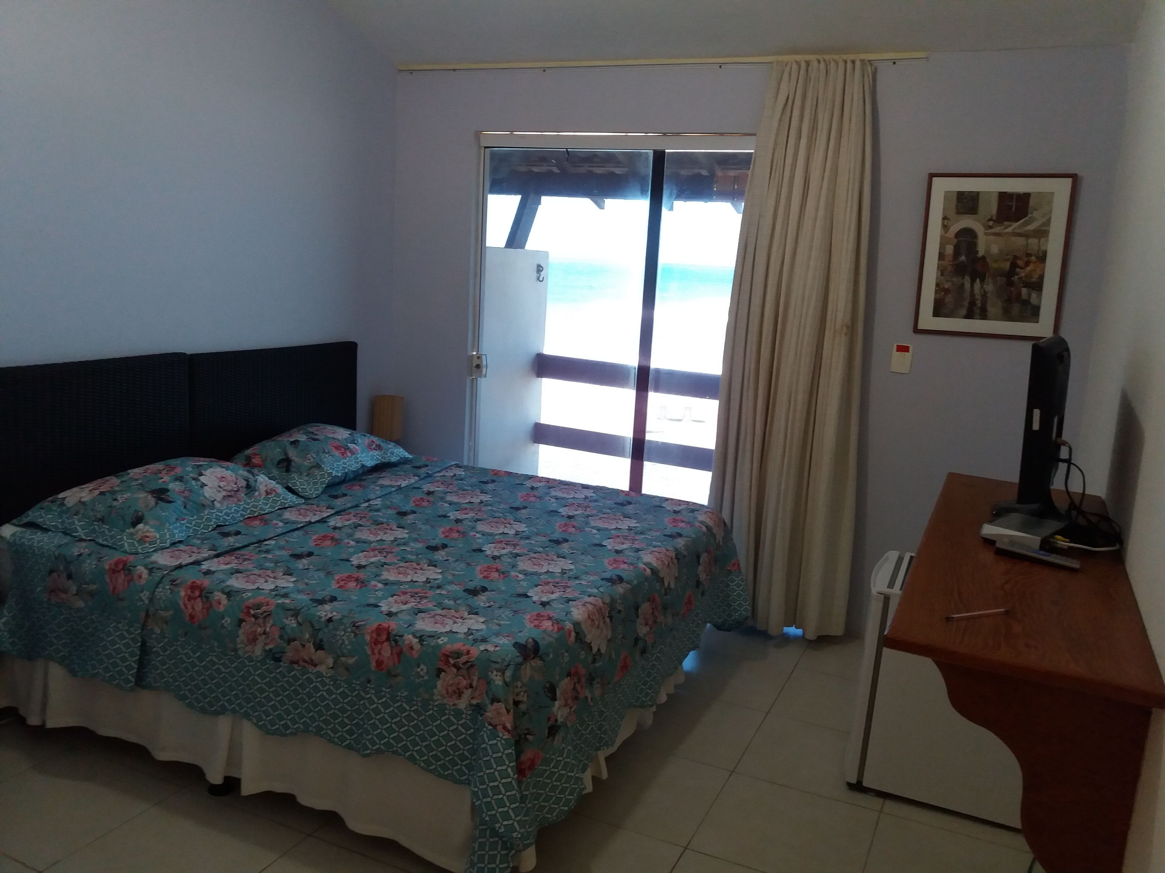 Un dormitorio con cama, escritorio, silla, ventana con cortinas y puerta.