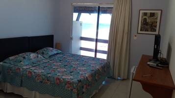 Un dormitorio con cama, escritorio, silla, ventana con cortinas y puerta.