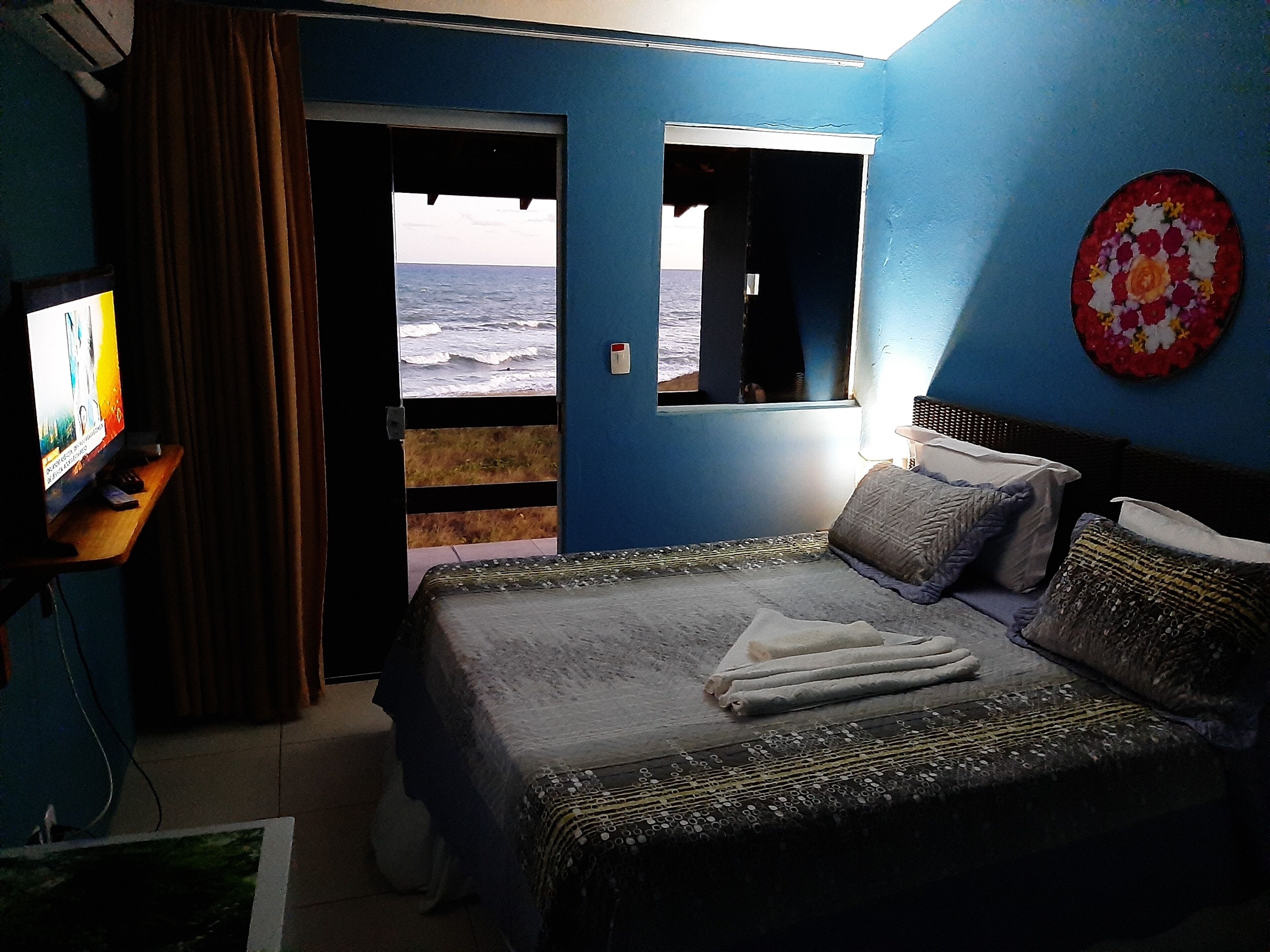 Una habitación con cama, televisión y ventana con vista al océano.