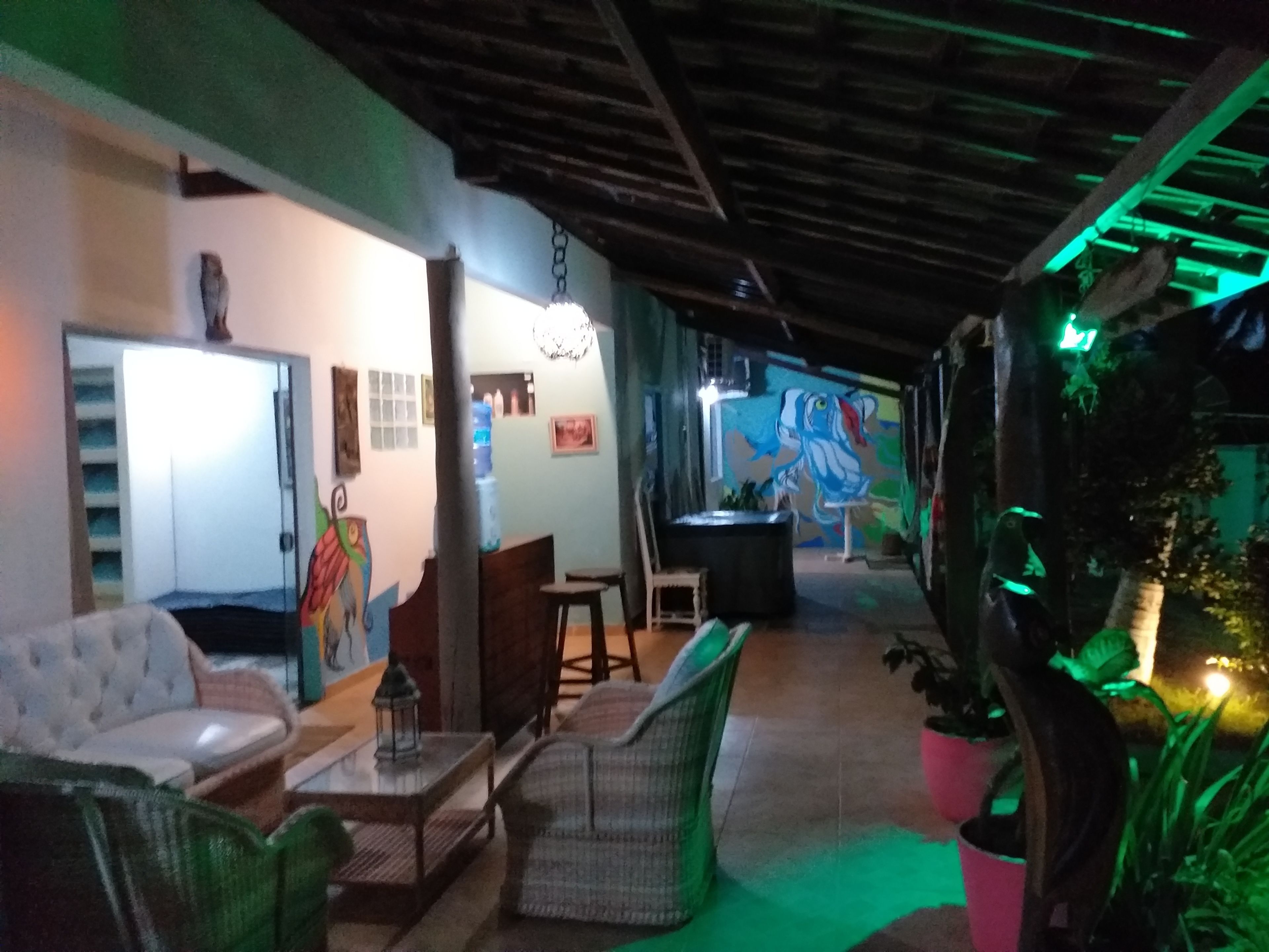 Un espacio interior acogedor con mobiliario de mimbre, un sofá y una mesa. Hay un mural en la pared y una planta en maceta a la derecha.