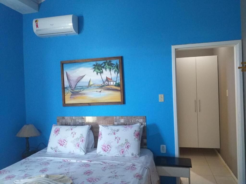 Un dormitorio con una cama, un cuadro de una playa, un aire acondicionado y una puerta a otra habitación.