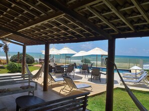 Ein überdachter Außenbereich mit Pool, Liegestühlen und Sonnenschirmen mit Blick auf den Ozean.