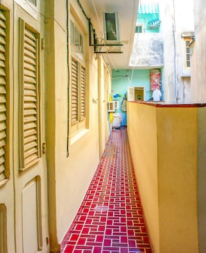 A narrow corridor with red-tiled flooring, beige walls, and shutters on the windows. - Casa Mildred (Havana)