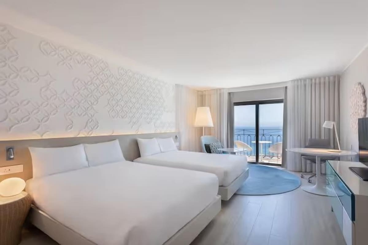 A hotel room with two beds, a balcony with a view, a desk with a chair, and a TV.