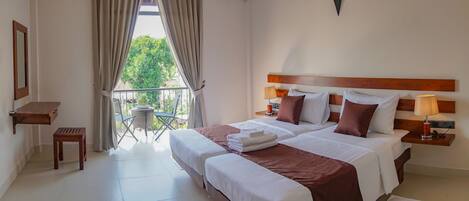 A hotel room with a large bed, a small balcony with a table and chairs, and an air conditioning unit on the wall.