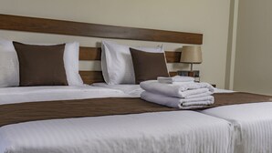 A neatly made bed with white and brown bedding, a lamp on a bedside table, and a stack of white towels. - Hive 68 - Hotel and Resorts Negombo (Negombo)