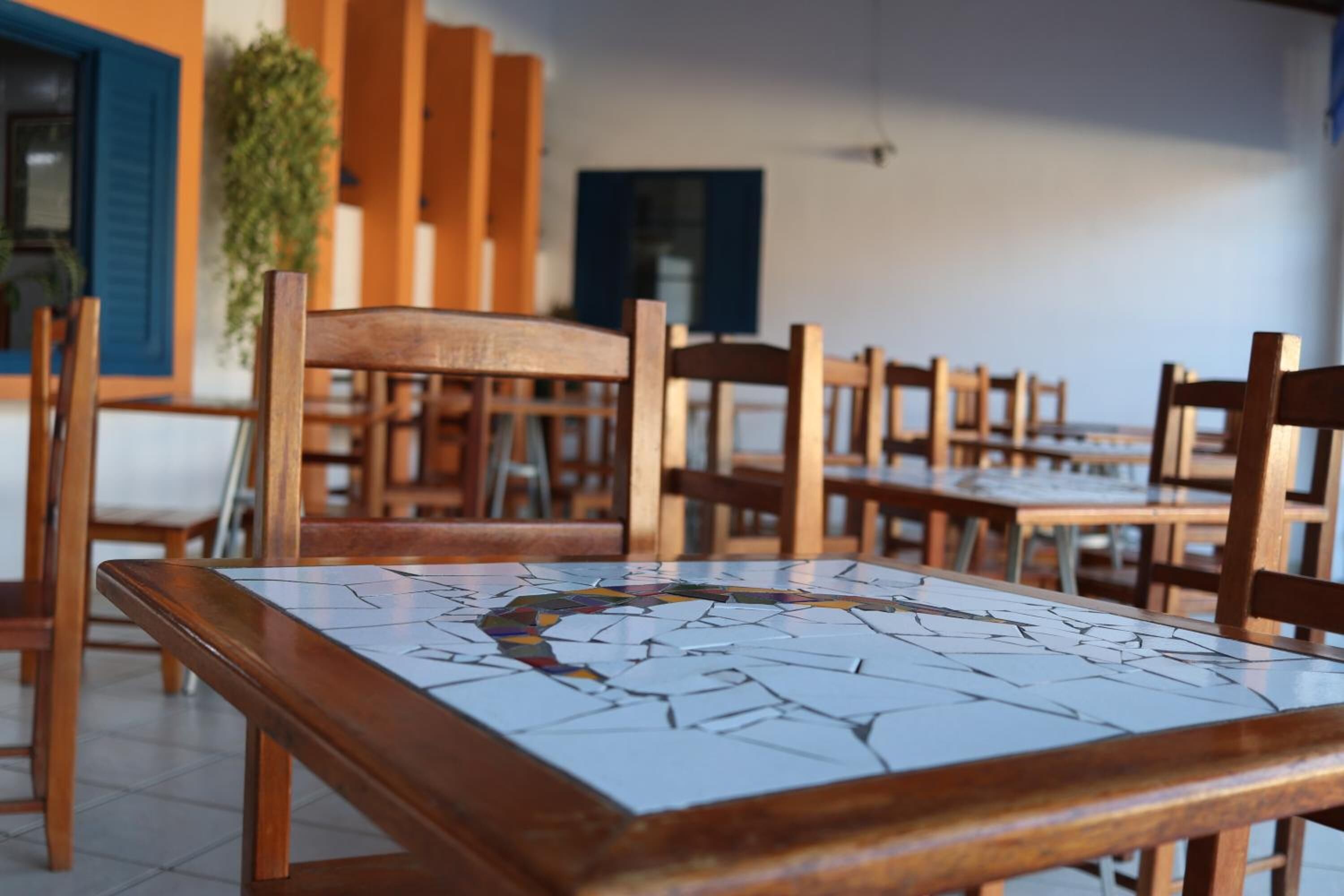 A dining area with wooden tables and chairs, a tiled floor, and a blue door in the background.
