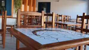Un comedor con mesas y sillas de madera, piso de baldosas y una puerta azul al fondo.