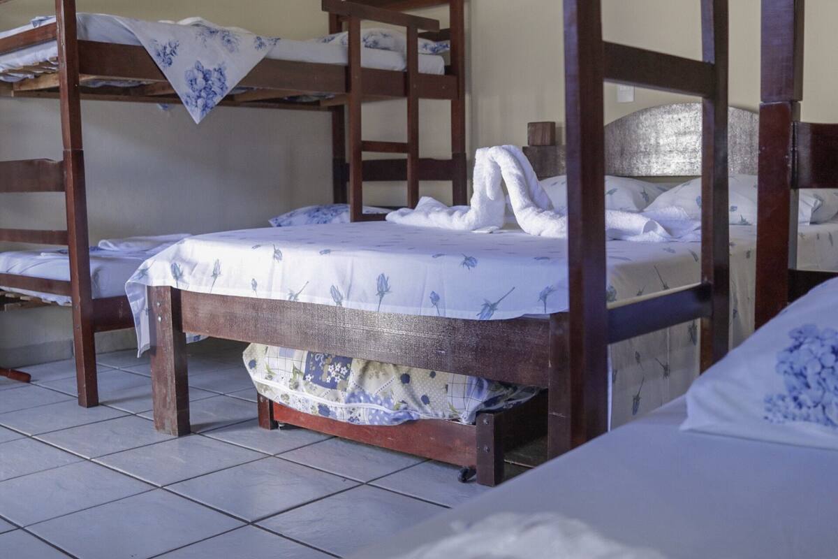 Une chambre avec un lit superposé, une couvre-lit à motifs floraux, une serviette blanche sur le lit et un sol carrelé.