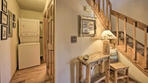 Ein Flur mit einem weißen Gerät, einer Holztreppe und einem rustikalen Tisch mit einer Lampe.