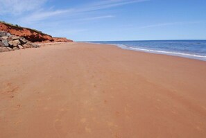 A wide sandy beach with a rocky cliff on the left and calm ocean waves on the right.
