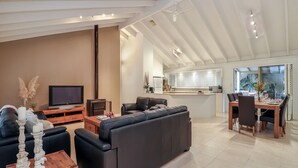 Ein modernes Wohnzimmer mit einer schwarzen Couch, einem Holztisch und einem Fernseher. Es gibt eine Küchenzeile mit einem Esstisch und Stühlen.
