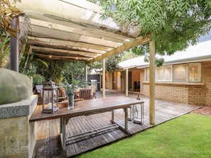 Un patio couvert avec une table et des chaises en bois, un barbecue et un bac à fleurs en pierre.