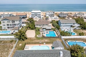 A coastal residential area with multiple houses, a large swimming pool, and a beach in the background. - Joy Seas | 265 ft from the beach | Private Pool (Virginia Beach)